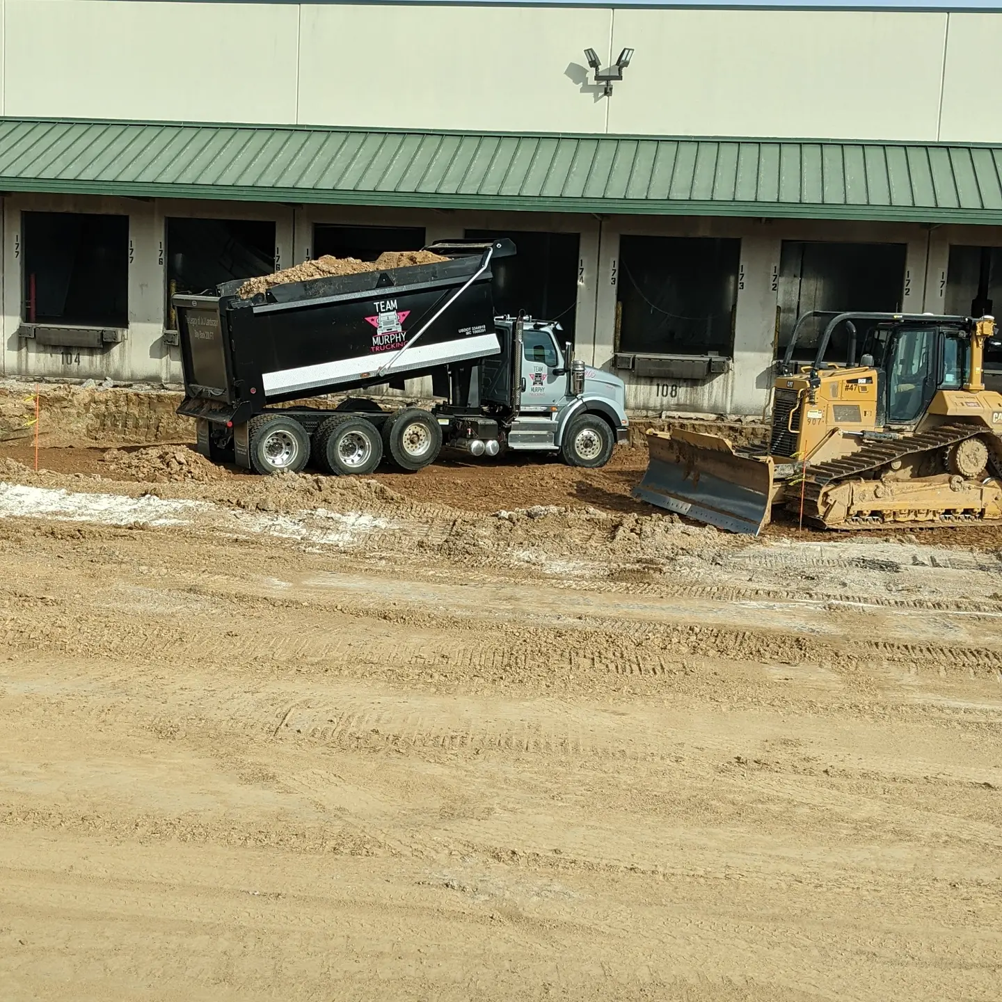 A dump truck and a tractor in the dirt.