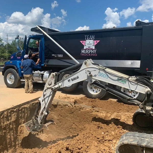 A dump truck is parked next to the back of a tractor.