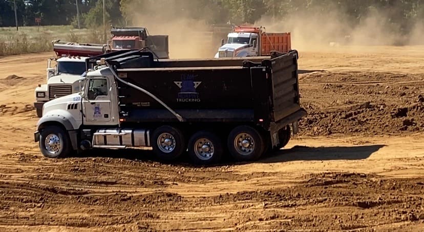 A dump truck is driving down the dirt road.